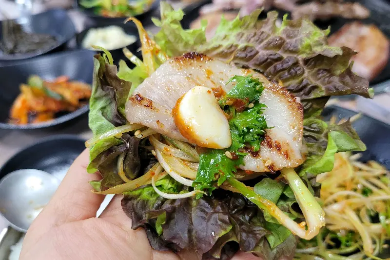 싱싱한 쌈채소에 돼지갈비를 싸서 먹는 모습
