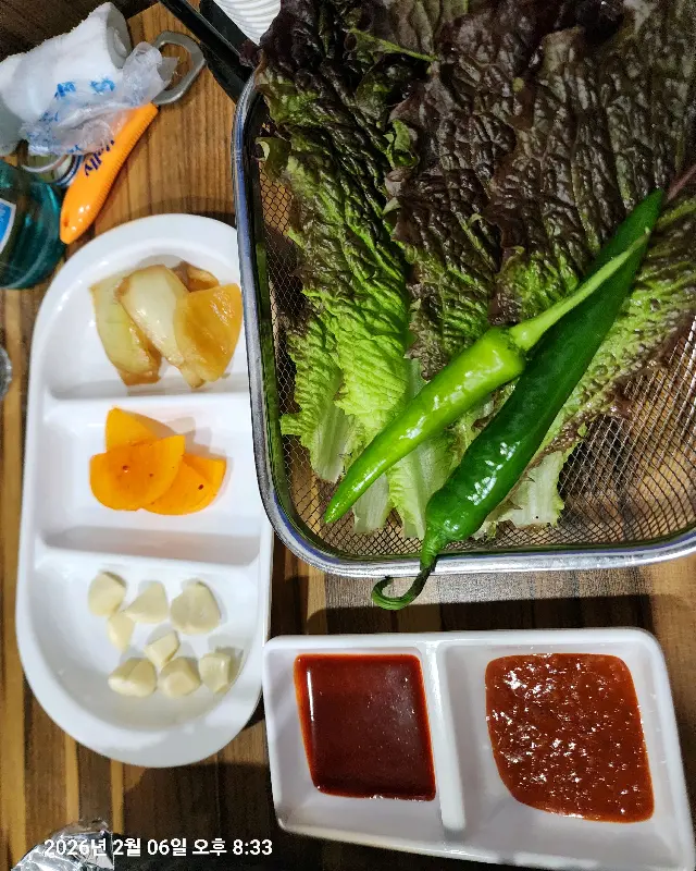 신선한 채소와 쌈장, 초고추장, 삶은 양배추, 단감 슬라이스가 담긴 밑반찬