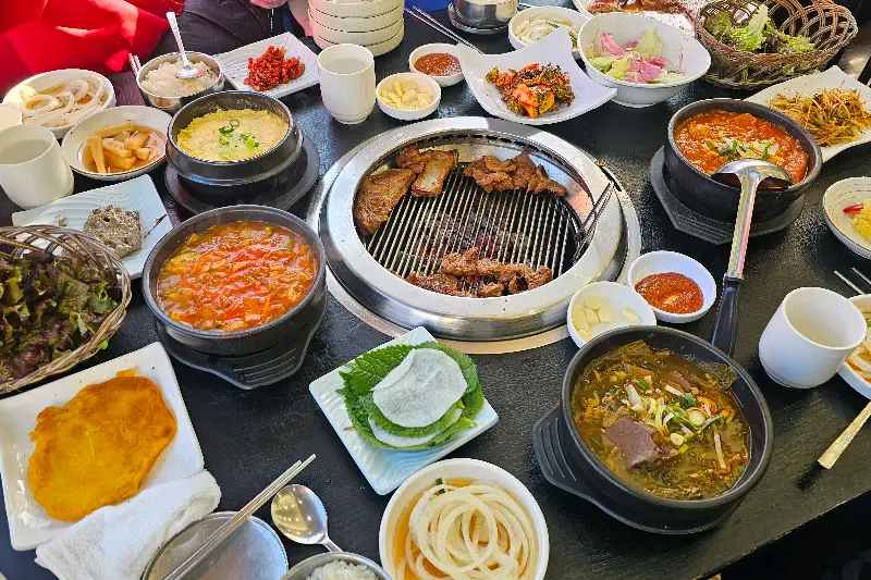 다양한 곁들임 찬과 돼지갈비가 숯불 위에 올려진 모습