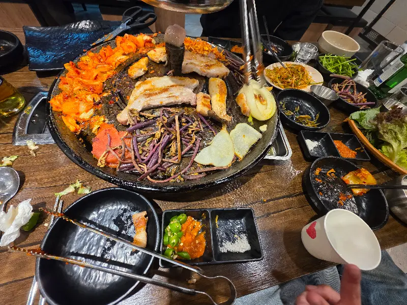 솥뚜껑 위에 푸짐하게 차려진 삼겹살과 반찬들