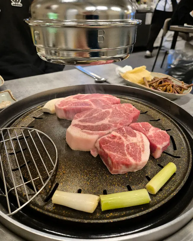 두툼한 삼겹살과 곁들여 먹을 채소, 특제 소스가 불판 위에 놓인 모습