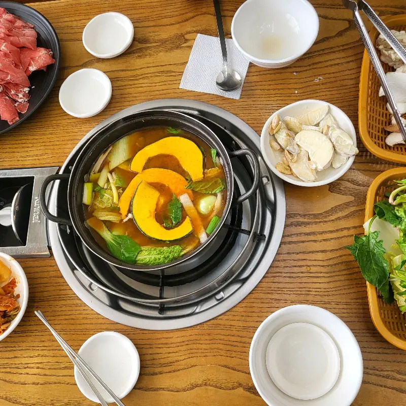 테이블 위에 놓인 샤브샤브 냄비와 각종 채소, 고기