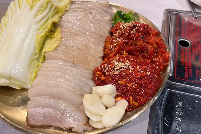 잘 삶아진 가브리살 수육과 김치, 배추, 마늘이 담긴 접시