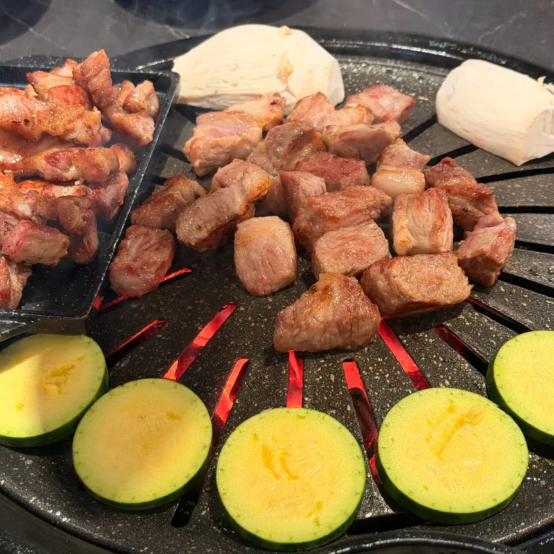 삼겹살과 미나리, 버섯, 떡을 함께 구워 먹는 모습