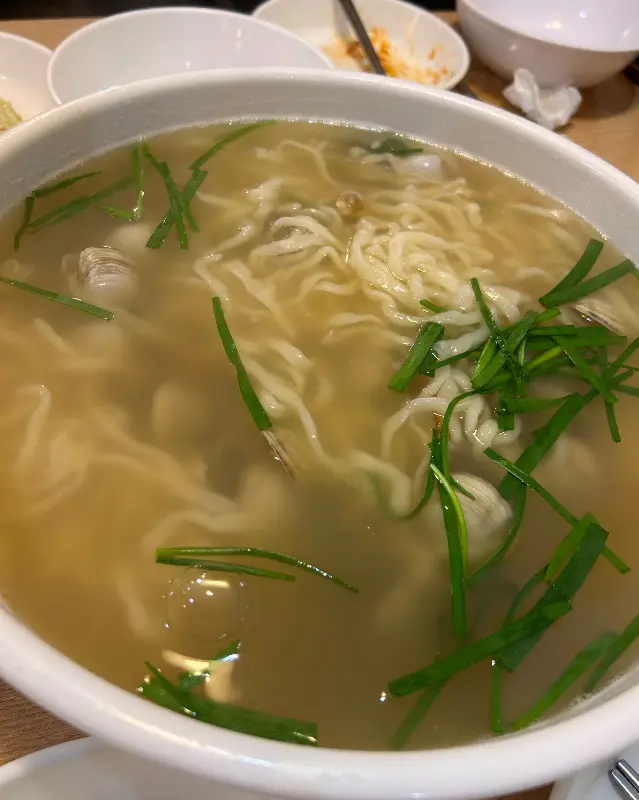 뽀얀 국물에 쫄깃한 면발이 담긴 칼국수 위로, 신선한 부추가 듬뿍 올려져 있어 보기만 해도 시원함이 느껴진다.