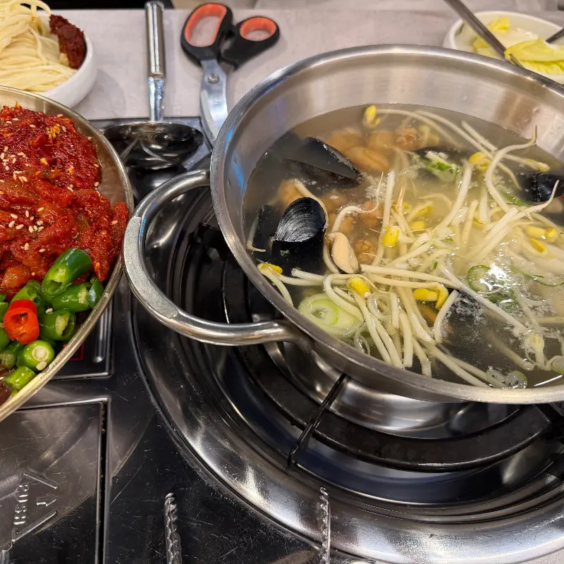 칼국수가 담긴 냄비와 보쌈, 김치, 고추 등이 담긴 접시가 놓인 테이블 전경