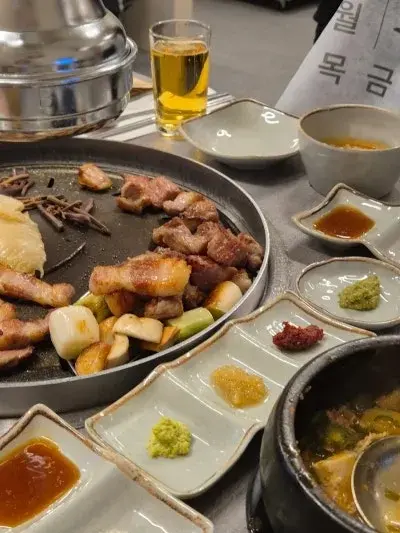불판 위에 구워진 고기와 꽈리고추, 다양한 소스, 찌개가 테이블 위에 놓인 모습