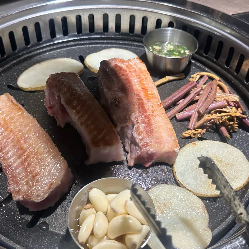 불판 위에 올려진 삼겹살, 마늘, 버섯