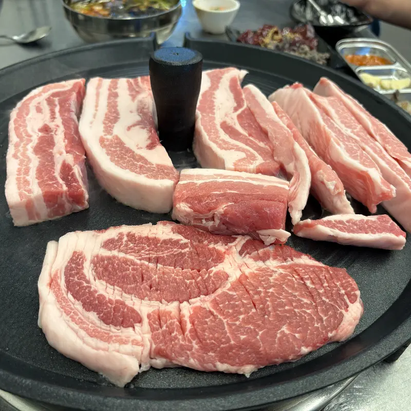 두툼한 삼겹살과 목살이 솥뚜껑 위에 올려져 있는 모습