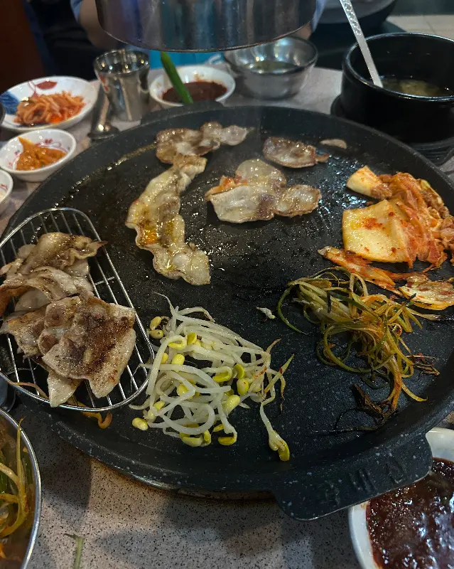 무쇠 솥에 구워지는 대패 삼겹살과 김치, 콩나물, 파절이