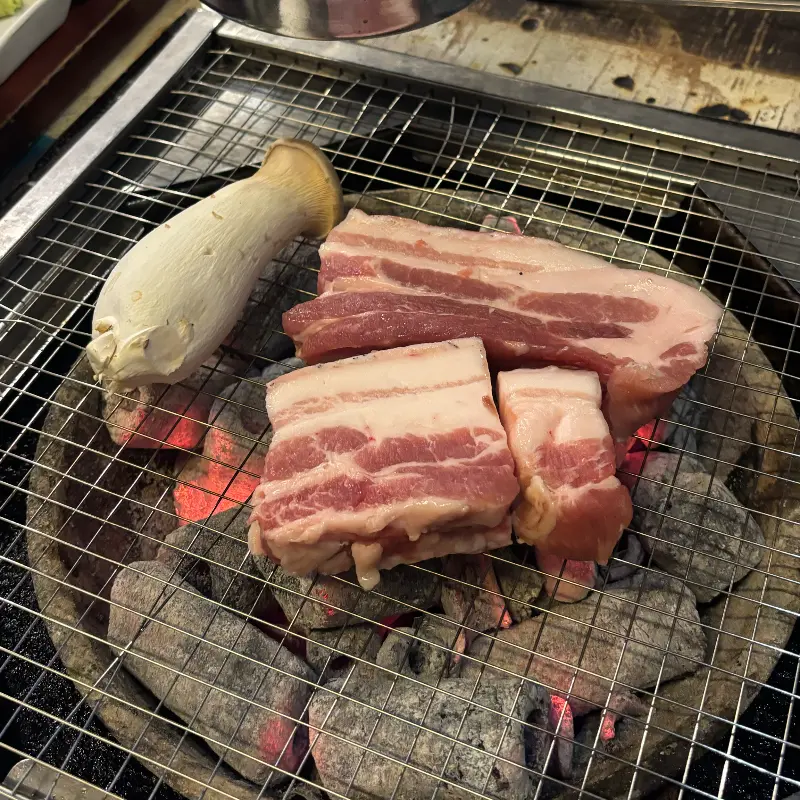 숯불 위에서 노릇하게 익어가는 오겹살과 버섯