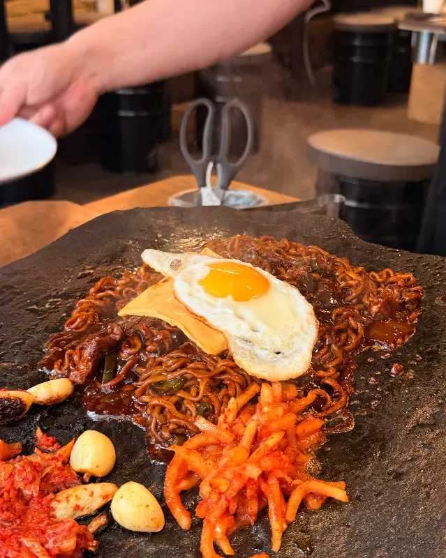돌판 위에 짜장면을 붓고 김치, 마늘, 계란후라이, 치즈를 올려 만든 돌판 짜파게티
