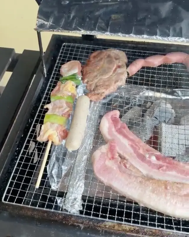 숯불 그릴에 고기, 소세지, 꼬치를 굽는 모습