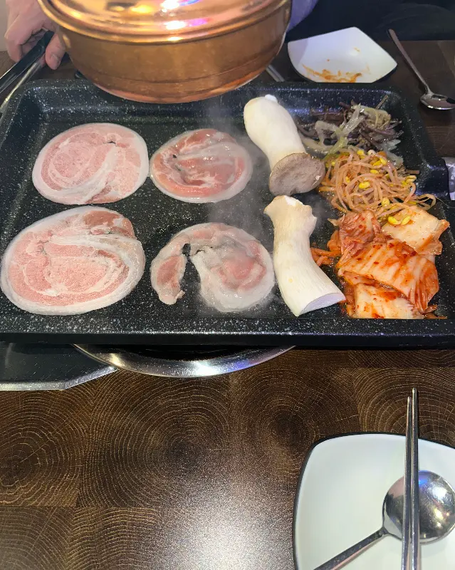 불판 위에서 익어가는 냉꽃삼겹과 김치, 콩나물