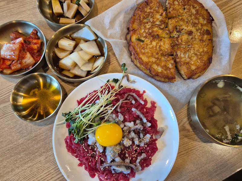 육회탕탕이와 녹두전, 그리고 다양한 밑반찬이 함께 차려진 테이블