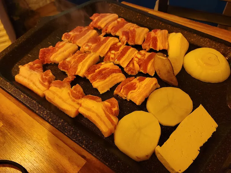 불판 위에서 노릇하게 익어가는 삼겹살과 감자, 버섯