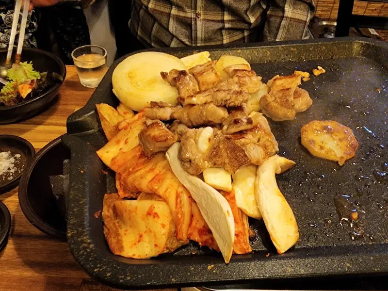 불판에 구워진 삼겹살과 김치를 젓가락으로 집는 모습