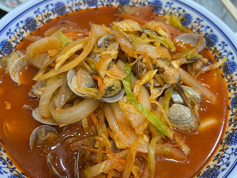 바지락과 오징어가 듬뿍 들어간 짬뽕의 모습. 국물은 붉은색을 띠고 있으며, 면발은 쫄깃해 보인다.