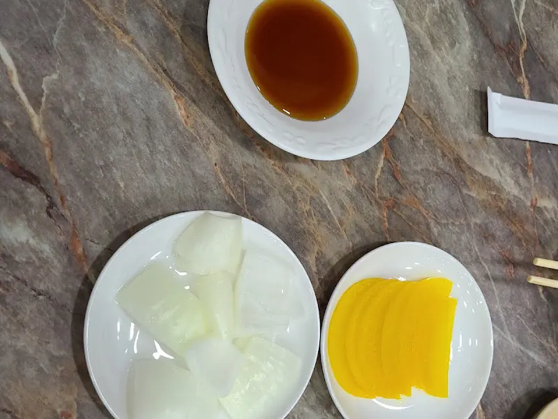 테이블 위에 놓인 탕수육 소스, 양파, 단무지의 모습. 소스는 갈색 빛깔을 띠고 있으며, 양파는 신선하고 아삭해 보인다.