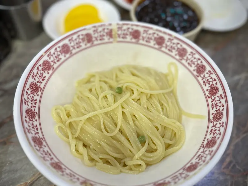 유니짜장 면 위에 짜장 소스를 부어 비비기 전의 모습. 면은 탱글탱글하고 윤기가 흐르며, 짜장 소스는 묽고 색깔이 옅은 편이다.