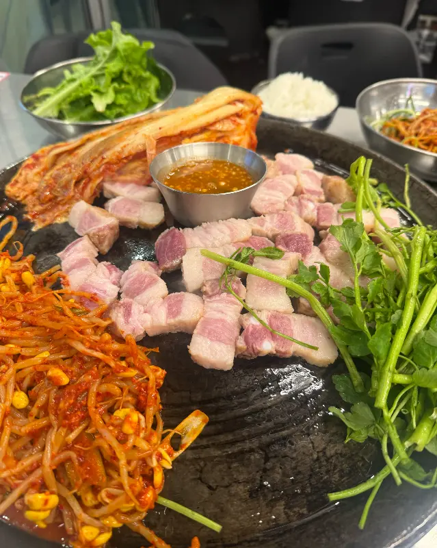 솥뚜껑 위에 올려진 삼겹살과 다양한 채소들