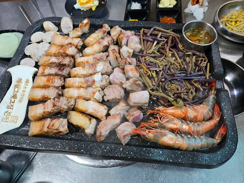 불판 위에 흑돼지 오겹살과 고사리, 새우, 소시지를 함께 구워 먹는 모습