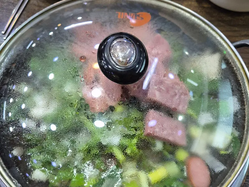 뚜껑이 덮인 채로 테이블에 놓인 부대찌개