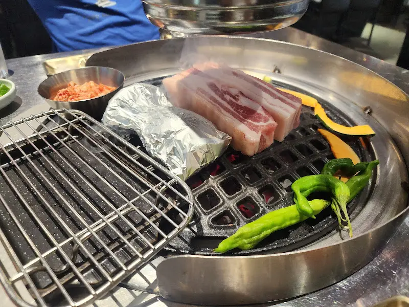 잘 구워진 숙성 삼겹살과 곁들임 채소들이 놓인 테이블 세팅