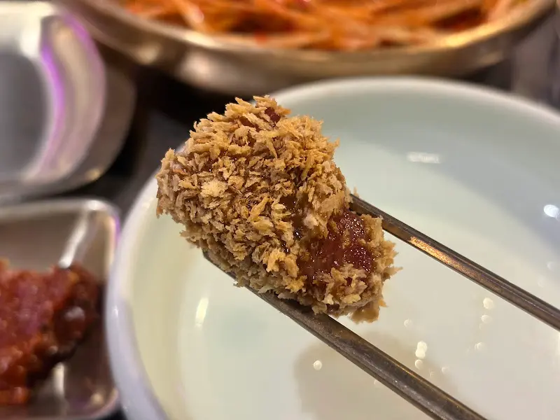 빵가루가 묻혀진 고기 한 점을 젓가락으로 들어올린 모습