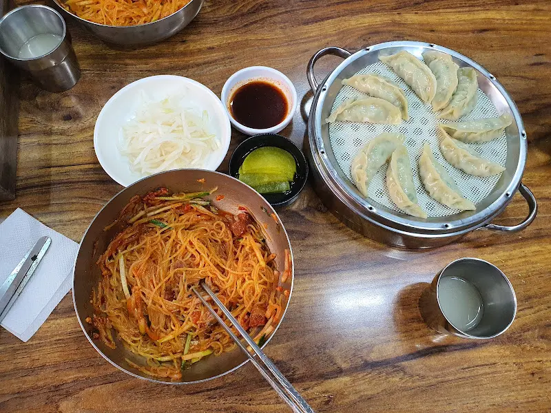 테이블 위에 놓인 밀면과 만두, 단무지