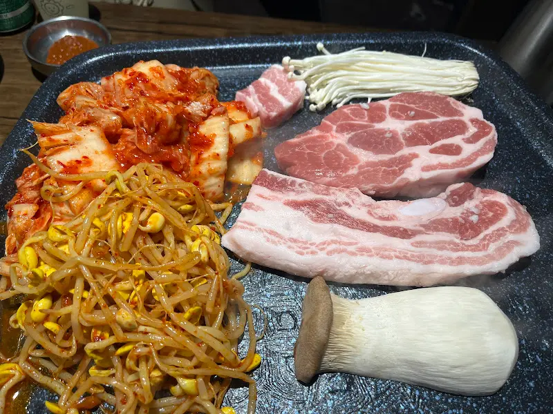 불판 위에 올려진 삼겹살, 김치, 콩나물