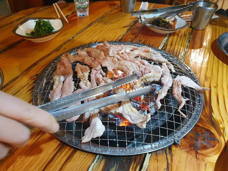 숯불 위에서 익어가는 닭목살을 집게로 굽는 모습