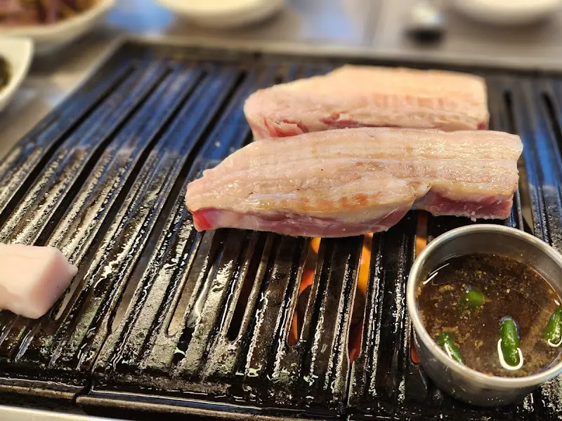 불판 위에서 맛있게 익어가는 흑돼지 오겹살과 멜젓