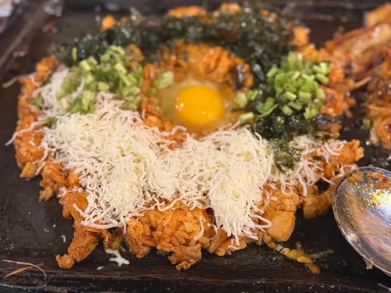 김치볶음밥 위에 뿌려진 치즈와 김가루, 계란 노른자의 조화