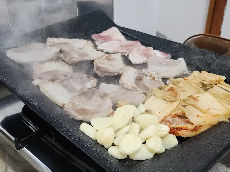 불판 위에서 맛있게 익어가는 냉삼과 김치, 마늘