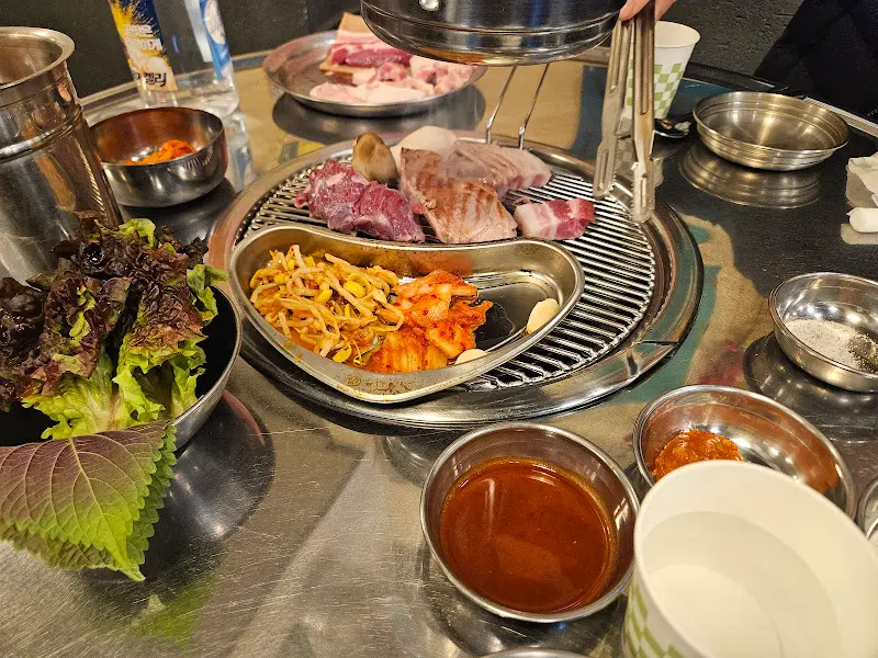 불판 위에 올려진 삼겹살, 김치, 콩나물의 조화