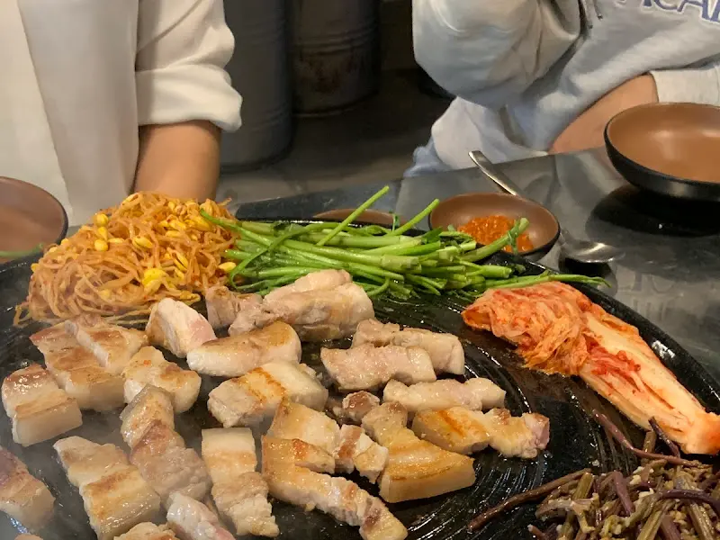 솥뚜껑 위에 구워진 삼겹살과 다양한 곁들임 채소