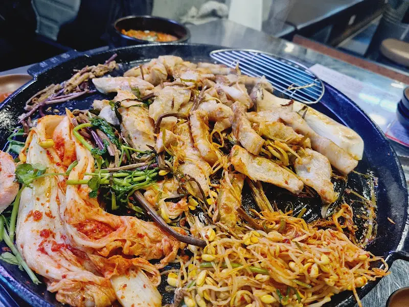 솥뚜껑에 가득 찬 삼겹살과 곁들임 채소