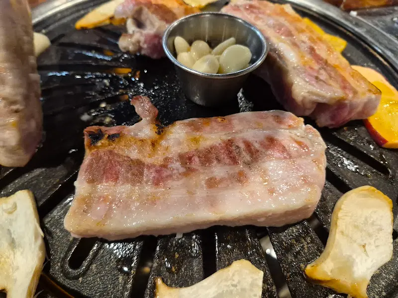 불판 위에서 노릇하게 구워지고 있는 삼겹살. 마늘과 버섯도 함께 구워 먹으면 더욱 맛있다.