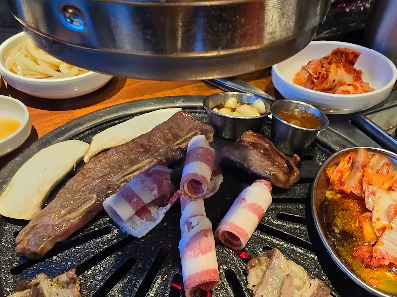 불판 위에 올려진 고기, 김치, 버섯, 마늘 등이 푸짐하게 담겨있다.