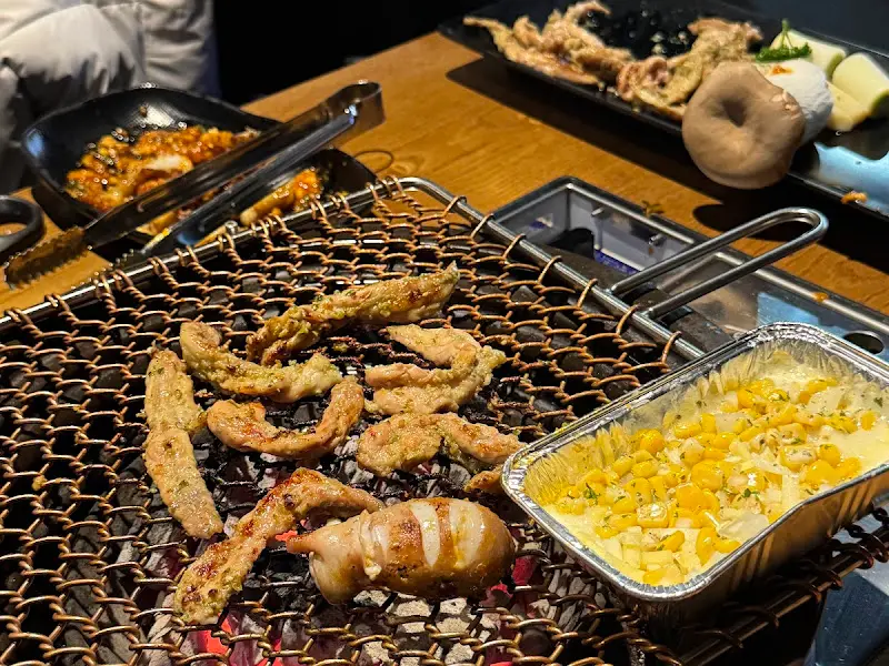 숯불 위에서 구워지는 닭목살과 콘치즈