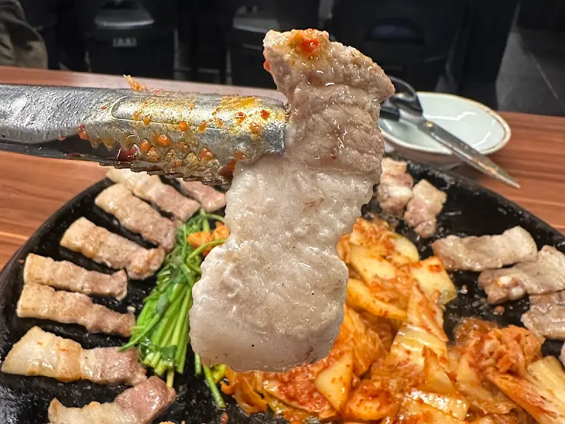 잘 구워진 삼겹살을 집게로 들어올린 모습