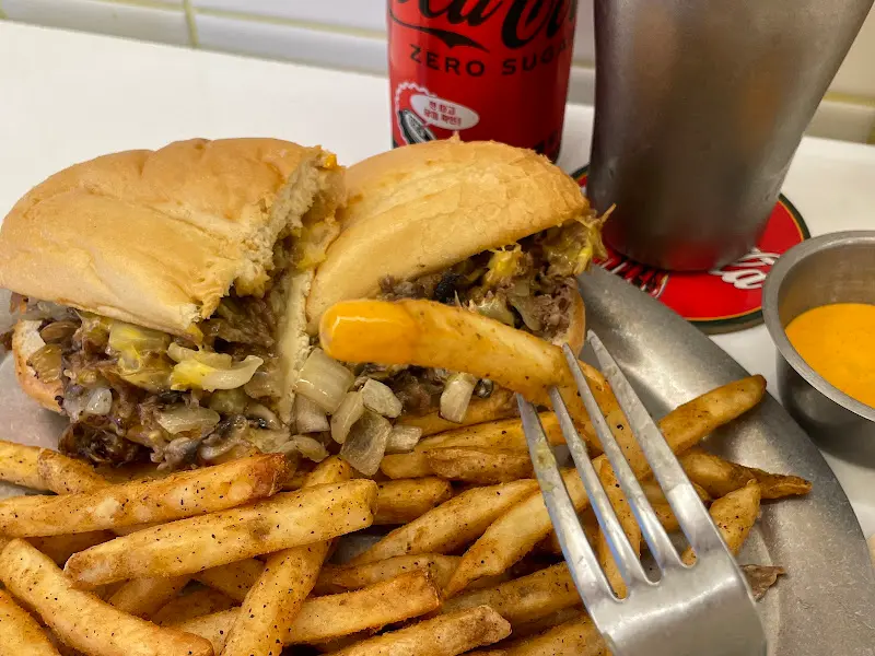 포크로 찍어 올린 필리 치즈 스테이크 샌드위치와 감자튀김