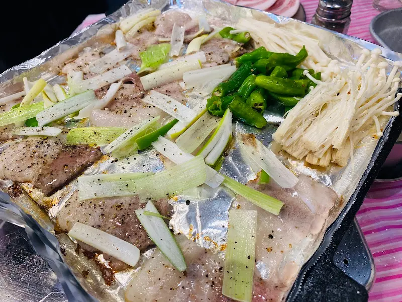 불판 가득 냉삼겹살과 대파, 버섯을 올려 구워 먹는 모습