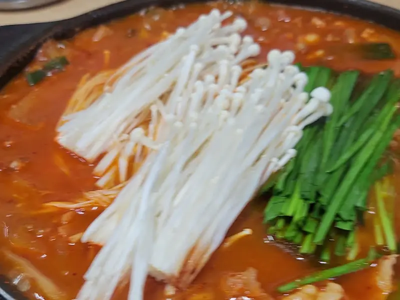 팽이버섯과 부추가 듬뿍 올려진 찌개의 모습