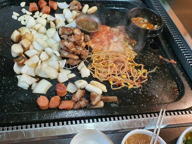 돌판 위에 구워진 삼겹살, 김치, 콩나물, 양파