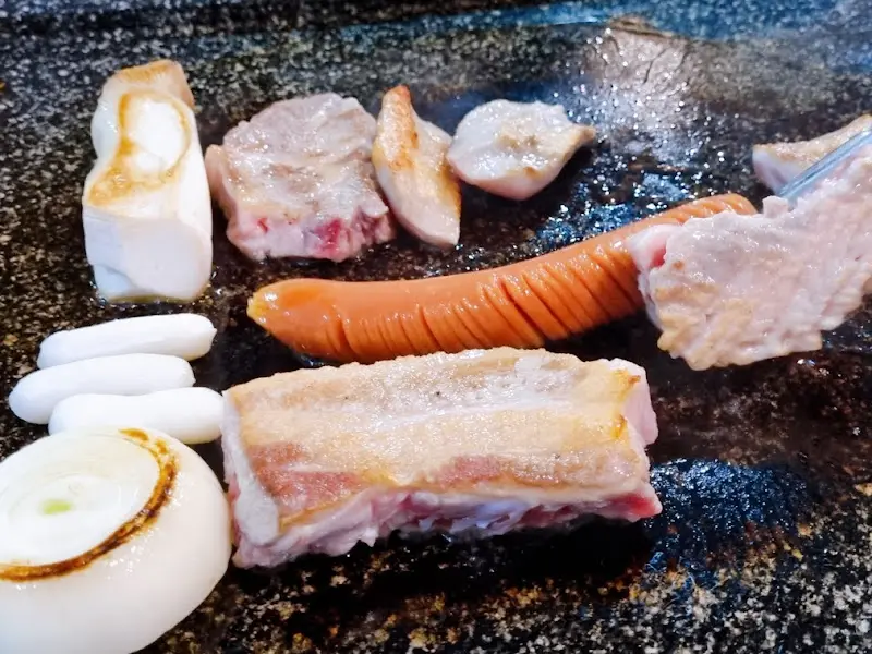 돌판 위에 올려진 삼겹살, 소시지, 떡, 양파