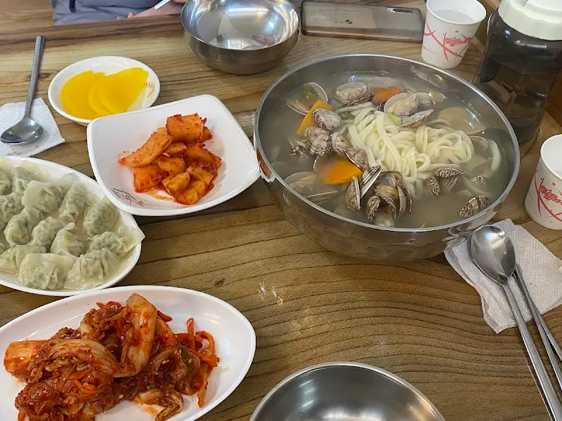 테이블 위에 놓인 칼국수와 반찬들 (김치, 깍두기, 오징어 젓갈)