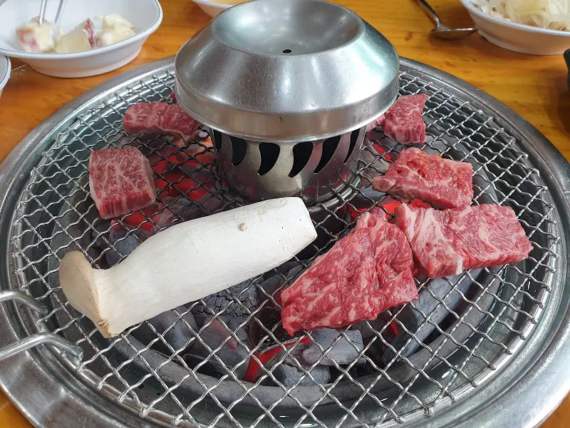 숯불 위에 올려진 고기와 버섯. 연기가 피어오르며 맛있는 냄새를 풍긴다.