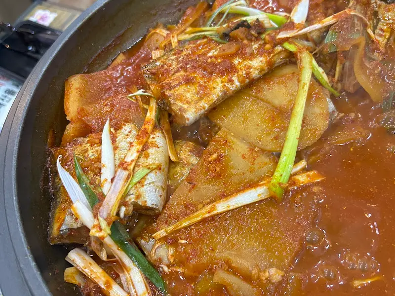 갈치조림이 담긴 냄비의 클로즈업 사진. 큼지막한 갈치와 무, 파가 보인다.